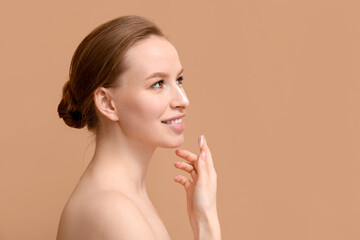Obraz na płótnie Canvas Young woman applying facial cream on brown background