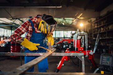 Worker wearing safety equipment while working on his welding machine. - obrazy, fototapety, plakaty
