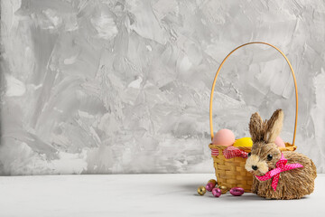 Toy Easter bunny and basket with painted eggs on table against grey background
