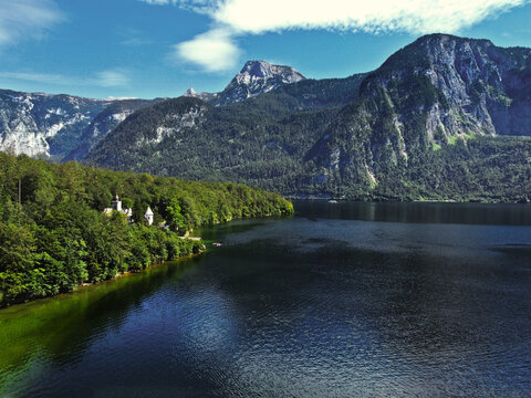 A lake and a mountain with green trees above the lake in the summer and on a beautiful sunny day