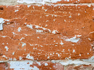 Close-up of a weathered red brick wall with peeling white paint. The rough texture of the bricks is contrasted by the smooth flakes of peeling paint.