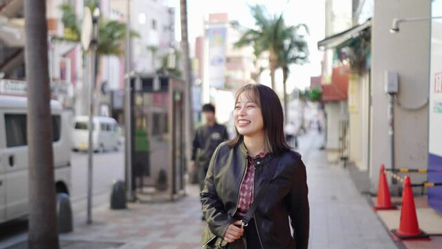 A young Japanese woman from Okinawa Prefecture in her 20s in winter clothes walking with a smile on Kokusai Street in Naha City, Okinawa Prefecture 沖縄県那覇市の国際通りで笑顔で歩く冬服の20代の沖縄県出身の若い日本人女性
