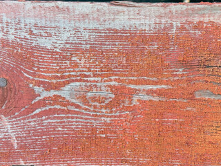 Close-up of a red wooden plank with visible wear and tear. The wood has a rough texture with deep cracks running along its surface.