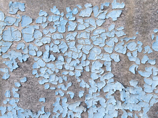 Close-up of peeling blue paint on a concrete wall. The rough texture of the concrete shows through the cracks and chips in the paint.