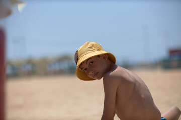 A boy on the beach in a yellow panama hat