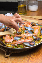 Hand serving shrimp and mussel paella with a wooden spoon from a pan, typical Spanish cuisine, Majorca, Balearic Islands, Spain