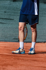 Close up of young boy with racket playing tennis on a clay court during a university tournament. the athlete is wearing a blue sports shirt.