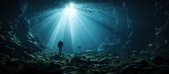 Tuinposter divers pass through a cave at the bottom of the deep sea © MBRAMO