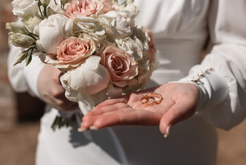 bride holds in hands wedding rings and bouquet