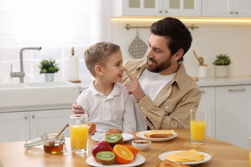 Father and his cute little son having fun during breakfast at table in kitchen - Powered by Adobe