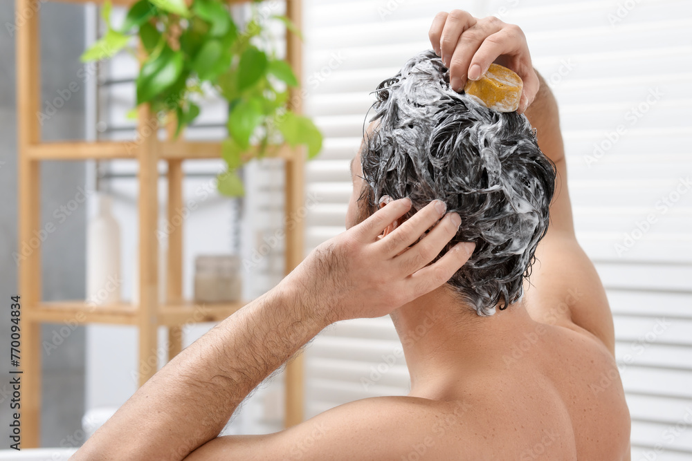 Poster man washing his hair with solid shampoo bar in bathroom, back view. space for text