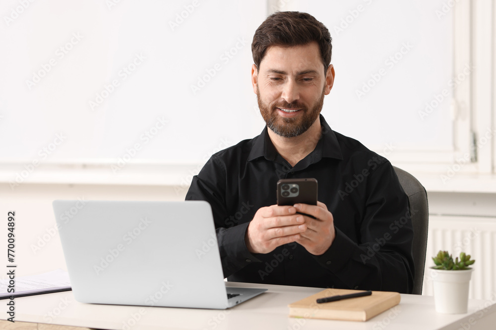 Poster smiling man using smartphone at table in office