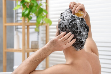 Man washing his hair with solid shampoo bar in bathroom, back view. Space for text