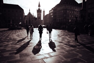 Silhouetted people walking in a city square with long shadows, dramatic lighting, and historic...