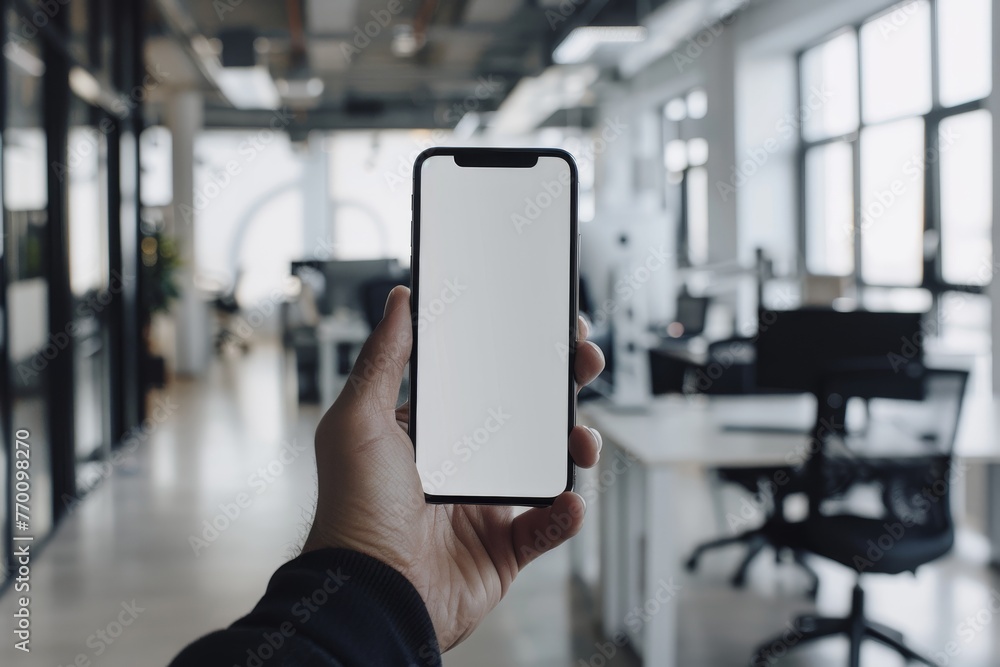 Wall mural a hand gripping a smartphone with blank screen ready for branding in a vibrant office