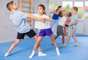 Preteen children practicing in pair self-defence movements with female trainer supervision