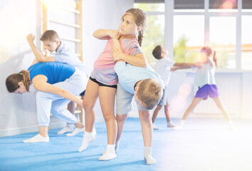 Fototapeta na wymiar Preteen children practicing in pair self-defence movements with female trainer supervision