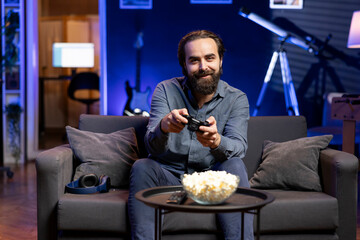 Portrait of smiling man playing videogame and eating snacks, holding controller. Cheerful gamer...