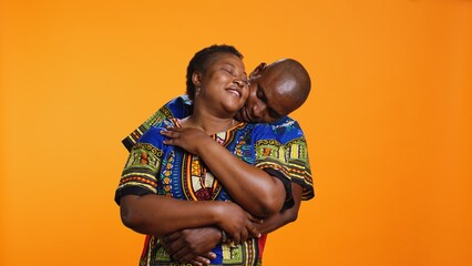 Sweet african american couple embracing in studio, holding each other and expressing their sincere feelings. Ethnic romantic man hugging his wife on camera over orange background.