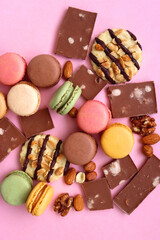 Pastel macarons, almond chocolate, peanut butter cookies and various nuts on bright pink background. Top view.