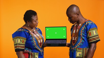 Ethnic people presenting laptop with greenscreen layout, showing blank mockup chromakey display and...