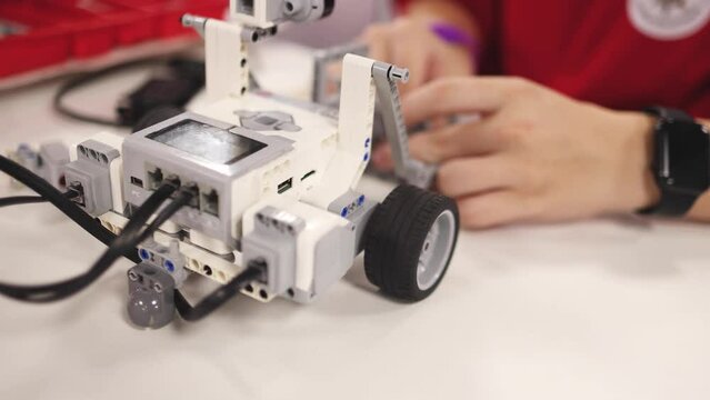 Group of diverse children kids with robotic vehicle model, close-up view on hands, science and engineering lesson in a classroom, making, coding and programming a robot in a school, robotics projects