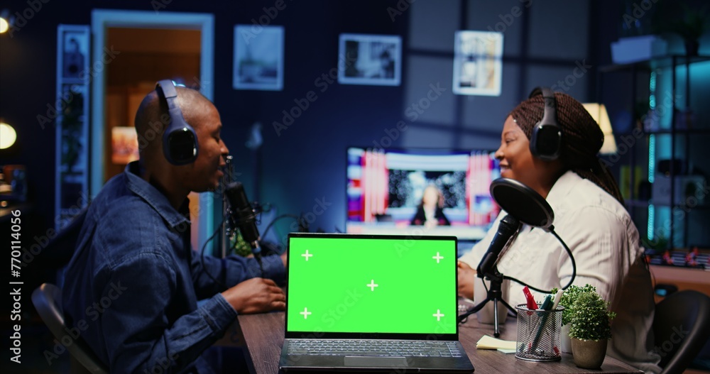Poster focus on green screen laptop in front of show host recording podcast, using analog mixer in studio. 