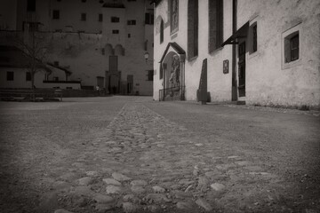 Cobblestone street leading to an old building with arched doorway, vintage black and white photo.