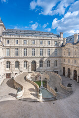 A double helix spiral staircase graces the cobblestone courtyard of the Louvre under a blue sky. Paris, France