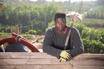 African male farmer in rubber gloves posing with a shovel in his garden