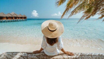 Fototapeta na wymiar Woman in straw hat sitting on beach view from above. Summer vacation at Maldives