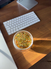 herbal tea with fruits is brewed in a transparent glass cup on the table, sunlight through the window beautifully illuminates the tea, a desktop with a laptop, monitor, wireless keyboard