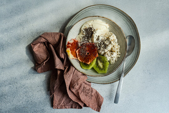 From above of nutritious breakfast bowl featuring creamy cottage cheese, natural yogurt, chia seeds, fresh kiwi slices, and a juicy wedge of Sicilian orange