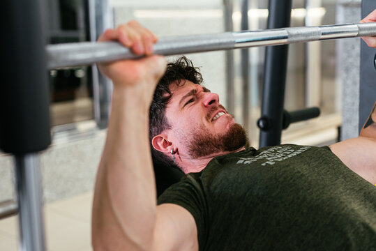 Young man exerting effort while bench pressing at gym