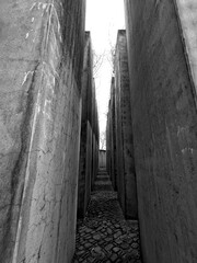 Narrow alley between tall concrete walls, black and white, symbolizing confinement or path leading to unknown.