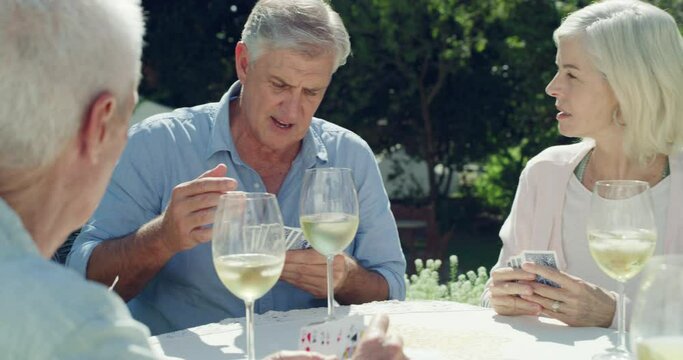 Old people, friends and playing cards or outdoor game for wine in backyard garden or entertainment, competition or party. Man, woman and table or glass alcohol at lunch or retirement, fun or social