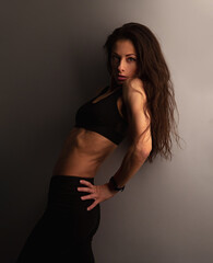 Sport sexy body beautiful slim woman with long hair posing in black sport bra showing the shoulders, abs, arms, standing on studio wall background with empty copy space. Healthy lifestyle vintage tone - 770148282