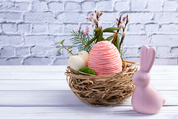 Easter nest with eggs and branches, bunny on the white table.