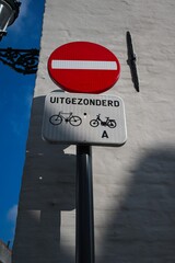 No entry traffic sign with an exception for bicycles, against a clear blue sky and white wall...