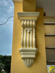 Classic white architectural column detail on a yellow wall under a clear sky, showcasing...