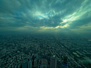 Aerial view of a cityscape under a dramatic cloudy sky with sunbeams piercing through clouds.