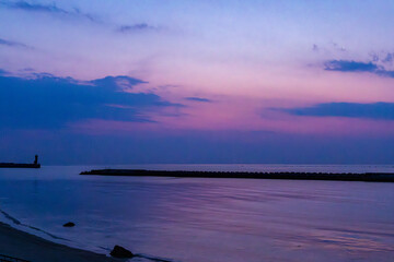 Blue hour falls over the ocean with pink clouds and a still waterbreak with beach in foreground
