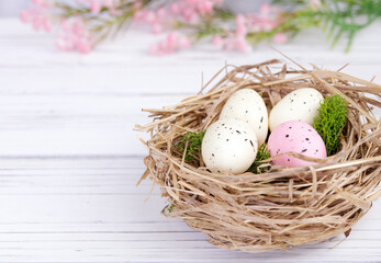 Easter decor with speckled eggs, nest and pink flowers.