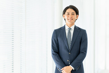 オフィスにいる笑顔のスーツ姿の若いアジア人男性ビジネスマン
