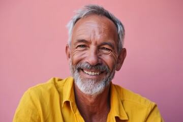 Portrait of a smiling senior man in yellow shirt on pink background