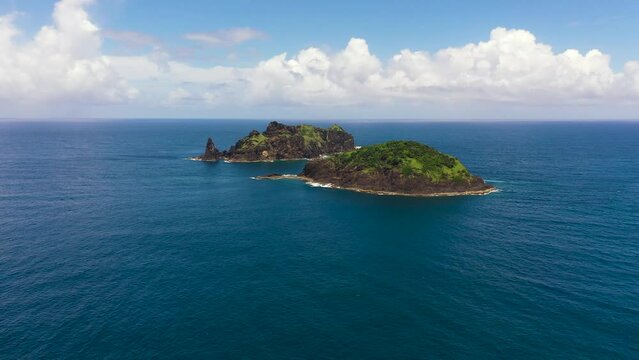 An island in a blue ocean against a background of blue sky and clouds. Dos Hermanos Island. Santa Ana, Cagayan. Philippines.