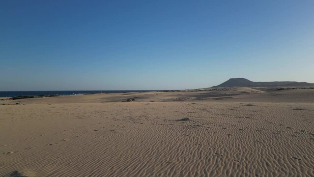 Expansive view of the Corralejo Dunes meeting the blue sea with mountainous backdrop in Fuerteventura