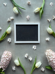 A blank blackboard picture frame surrounded by a variety of spring tulip flowers and hyacinth.