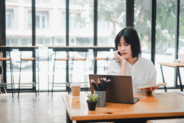 Young woman is deeply engrossed in her work on a laptop at a wooden table in a bright, modern cafe...