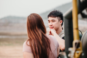 Tender scene as a woman gazes at a man, capturing an intimate, heartfelt exchange by their rugged car outdoors.